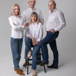 Atelier fotograficzne Duet Maciej Bazylewicz - Portret rodzinny: Dwie kobiety i dwóch mężczyzn w białych koszulach i jeansach pozują na jasnoszarym tle. Jedna z kobiet siedzi na czarnym stołku.