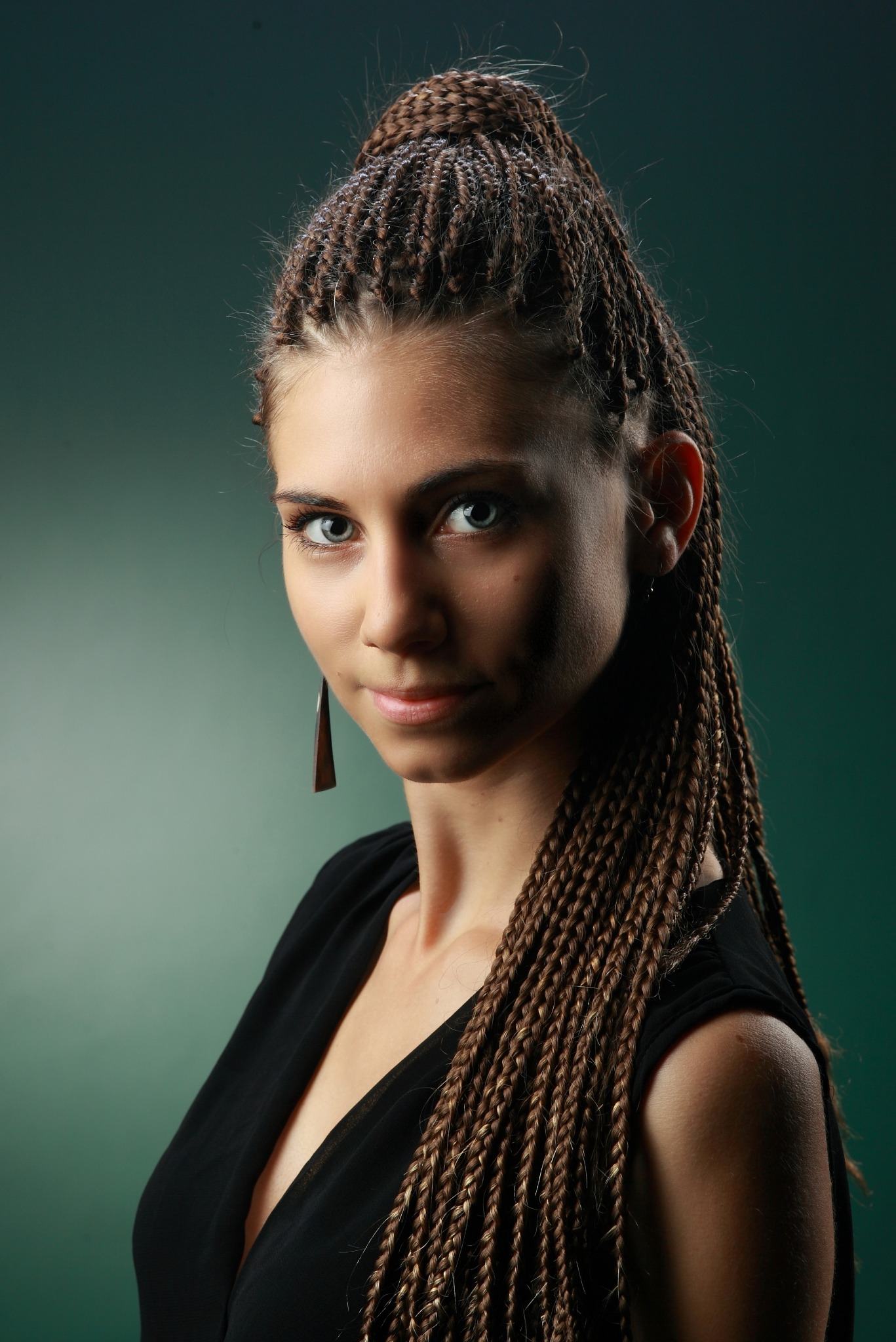 Portret młodej kobiety z zaplecionymi warkoczykami w odcieniach brązu, upiętymi częściowo na czubku głowy, w czarnej bluzce na tle zielonym. Widoczny kolczyk w geometrycznym kształcie.