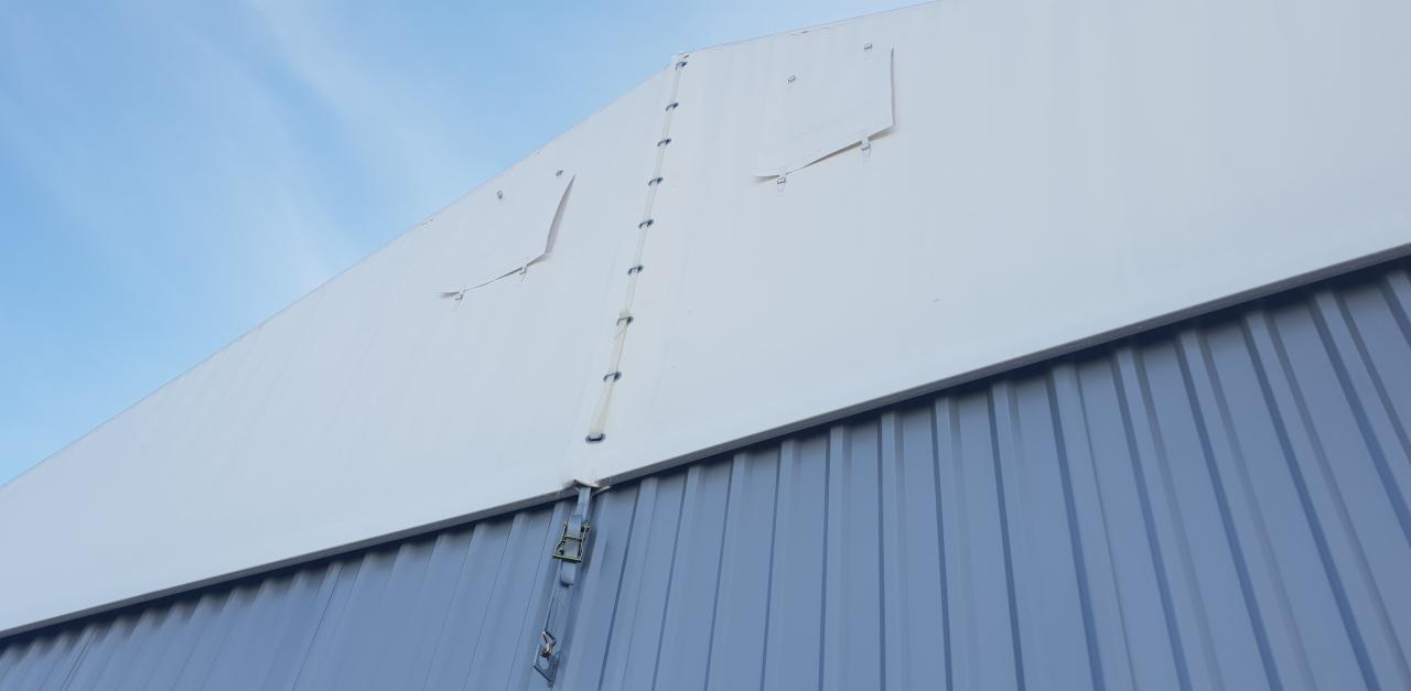 Szczegółowe ujęcie fragmentu hali z widocznym uszkodzeniem poszycia i elementami mocującymi na tle błękitnego nieba.