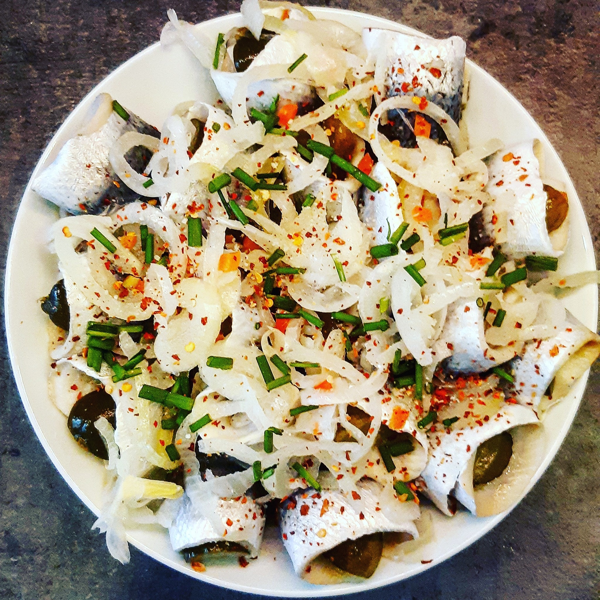 Rolmopsy z cebulą, ogórkiem i przyprawami na białym talerzu, widok z góry, na szarym tle.