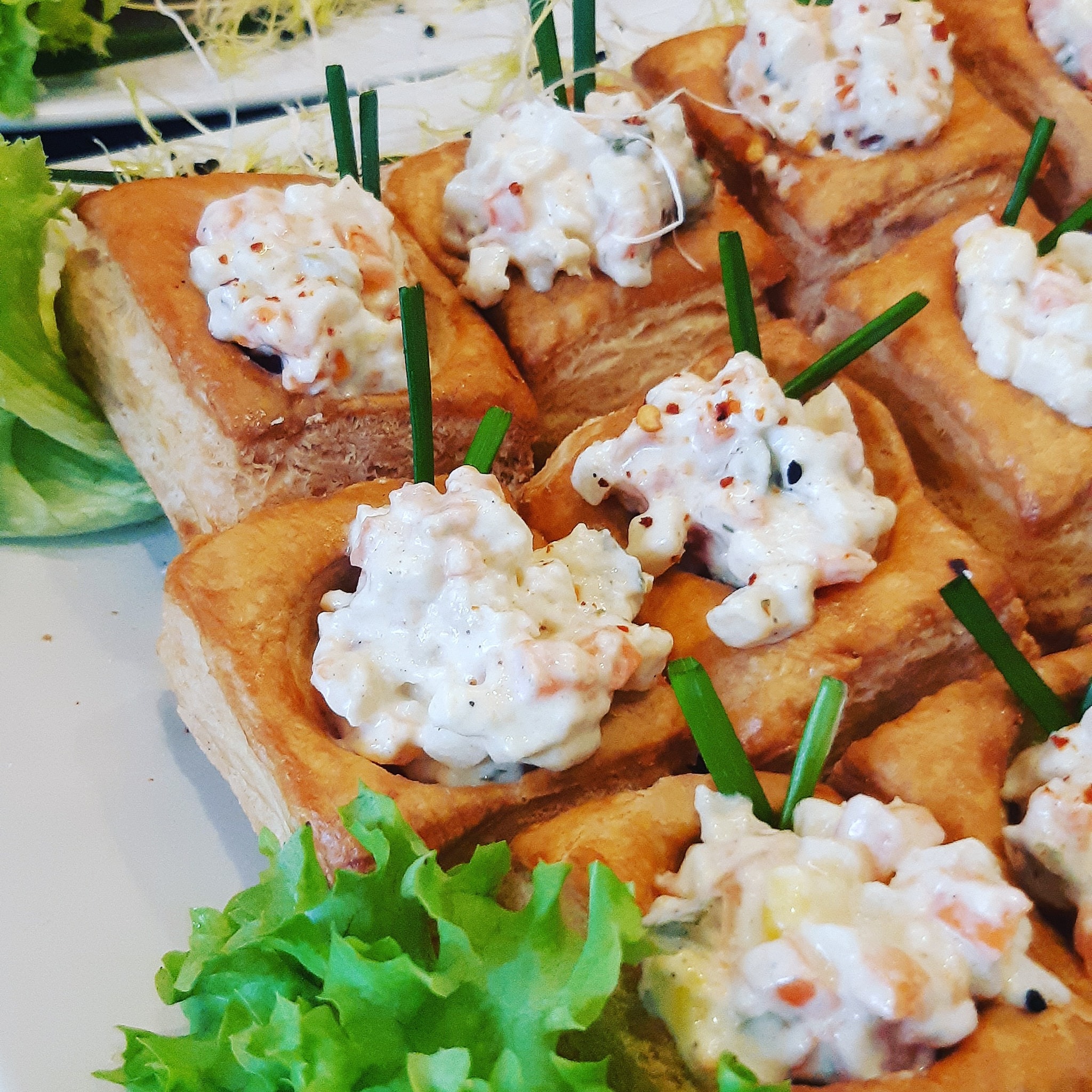 Kruche babeczki z kremowym farszem z kawałkami warzyw i szczypiorkiem, ułożone na białym talerzu z dekoracją z sałaty.