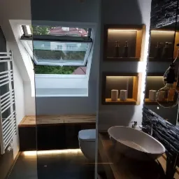 Nowoczesna łazienka na poddaszu z oknem dachowym, podświetlaną ławką z drewna, wolnostojącą wanną i ścianą z dekoracyjnego kamienia łupkowego.