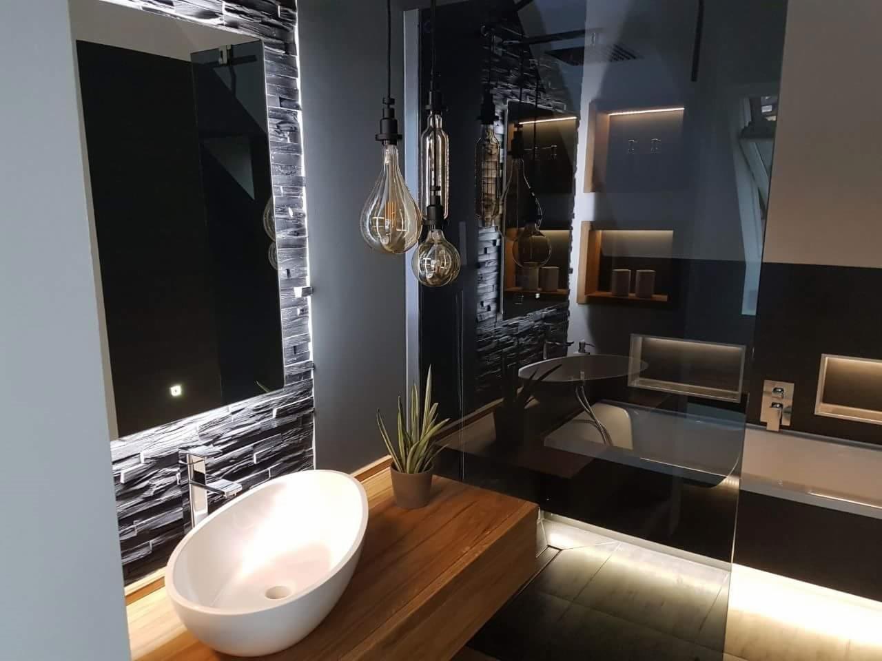 Nowoczesna łazienka z umywalką nablatową, lustrem z podświetlaną ramą z kamienia dekoracyjnego i wiszącymi lampami w stylu industrialnym.