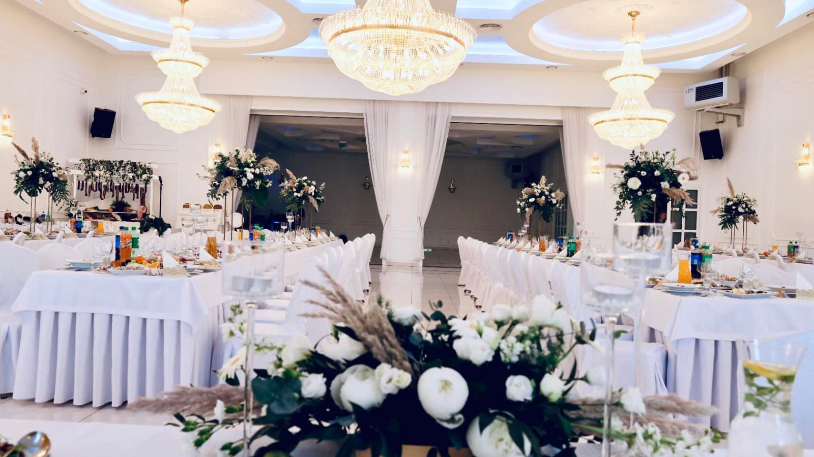 Uroczysta sala bankietowa w Tuszynie przygotowana na przyjęcie, z długimi stołami w białych obrusach, eleganckimi kompozycjami kwiatowymi i kryształowymi żyrandolami.