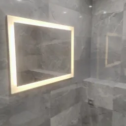 Nowoczesna łazienka wykończona szarymi płytkami imitującymi marmur, z podświetlanym lustrem w kształcie kwadratu i półką wbudowaną w ścianę.