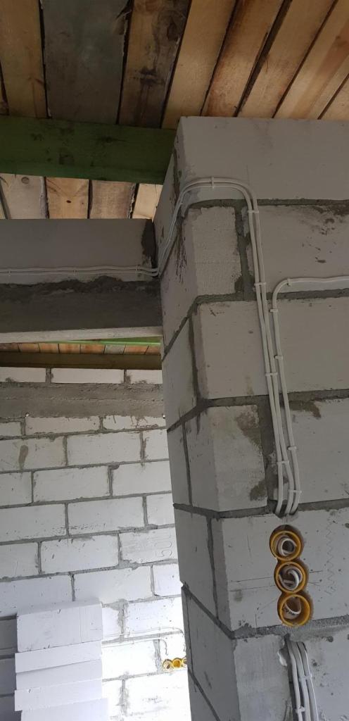 Białe przewody elektryczne prowadzone po ścianie z bloczków w surowym wnętrzu budynku w Warszawie, z widocznymi puszkami instalacyjnymi.