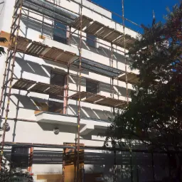 Elewacja budynku w Lubsku w trakcie tynkowania, widoczne rusztowania i fragmenty świeżo nałożonego tynku.