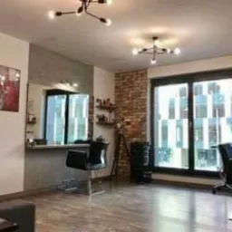 Jasne wnętrze salonu z nowoczesnym wystrojem: stanowiska pracy z lustrami, czarne krzesła, dekoracyjna ściana z cegły i designerskie lampy sufitowe.