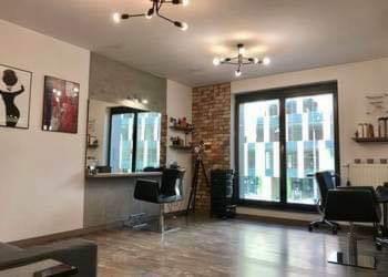 Jasne wnętrze salonu z nowoczesnym wystrojem: stanowiska pracy z lustrami, czarne krzesła, dekoracyjna ściana z cegły i designerskie lampy sufitowe.