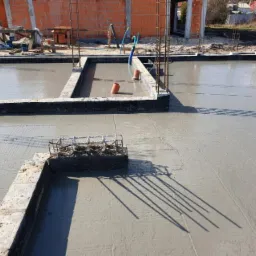 Wylany fundament z widocznym zbrojeniem i szalunkiem, surowy stan pod budowę domu z cegły ceramicznej.