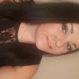 Uśmiechnięta kobieta z ciemnymi włosami i koronkową bluzką, patrząca w obiektyw, z delikatnym srebrnym naszyjnikiem.