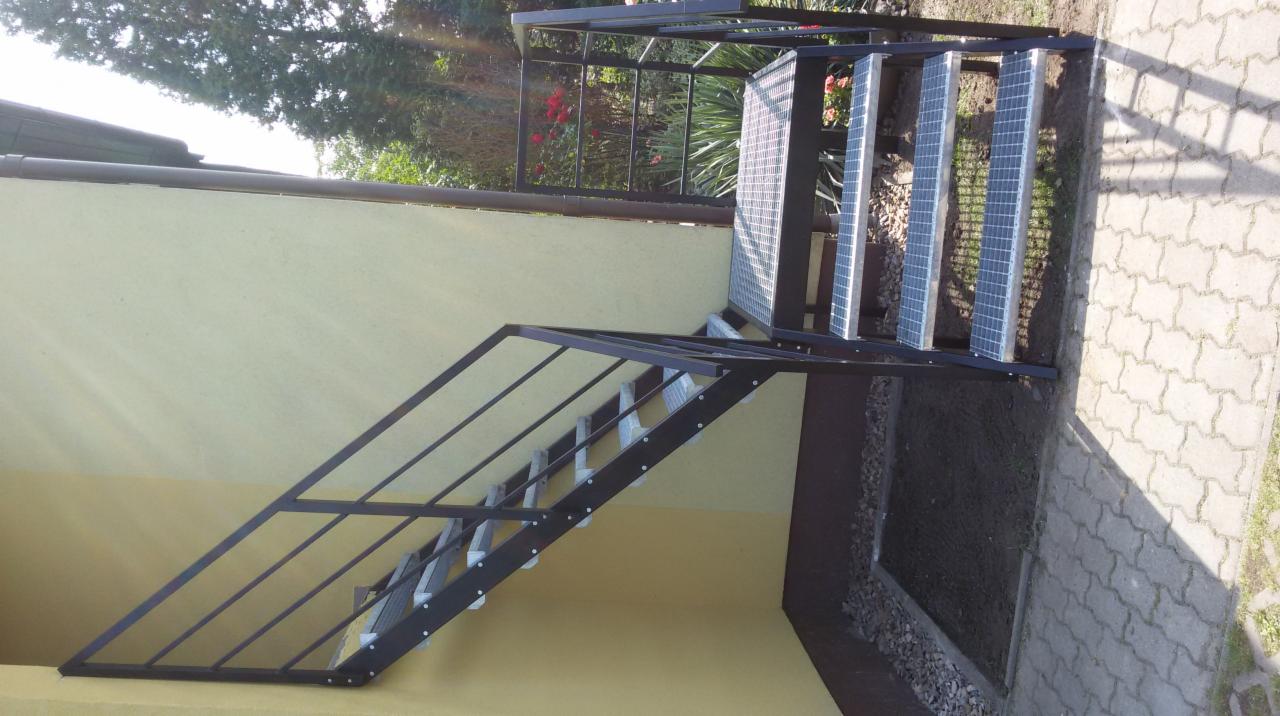Zewnętrzne schody metalowe z kratowymi stopniami i prostą balustradą w Sulęcinie, prowadzące na podwyższony teren.