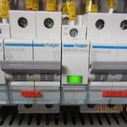 Szczegółowe ujęcie rozdzielnicy elektrycznej z wyłącznikami firmy Hager, widoczne oznaczenia SVN 121, MCN 202E, MBN 206E, etykiety HCL, FCWU, FSA-R oraz zielona dioda sygnalizacyjna.