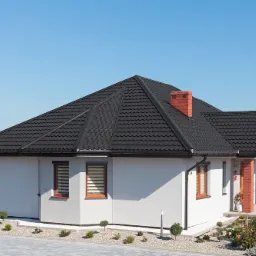 Dom jednorodzinny z ciemnym, nowym pokryciem dachowym z blachy na rąbek stojący, ceglanym kominem i białymi ścianami, otoczony zadbanym ogrodem i kostką brukową.