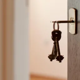 Klucze wiszące w zamku w drewnianych drzwiach, widoczne rozmyte wnętrze mieszkania w tle.
