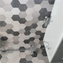 Ukończona łazienka z wanną, armaturą i heksagonalnymi płytkami w odcieniach szarości na ścianie.