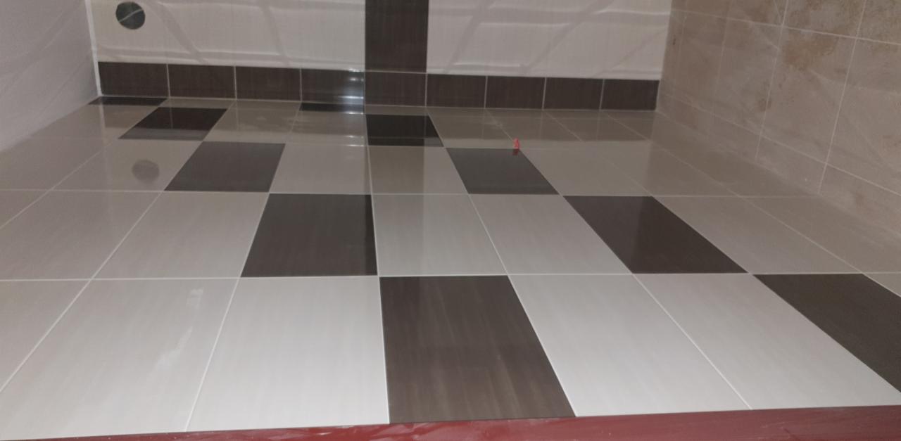 Ukończona podłoga w łazience z ułożonymi na przemian białymi i brązowymi płytkami, widoczne fragmenty ścian wykończonych w podobnej kolorystyce.