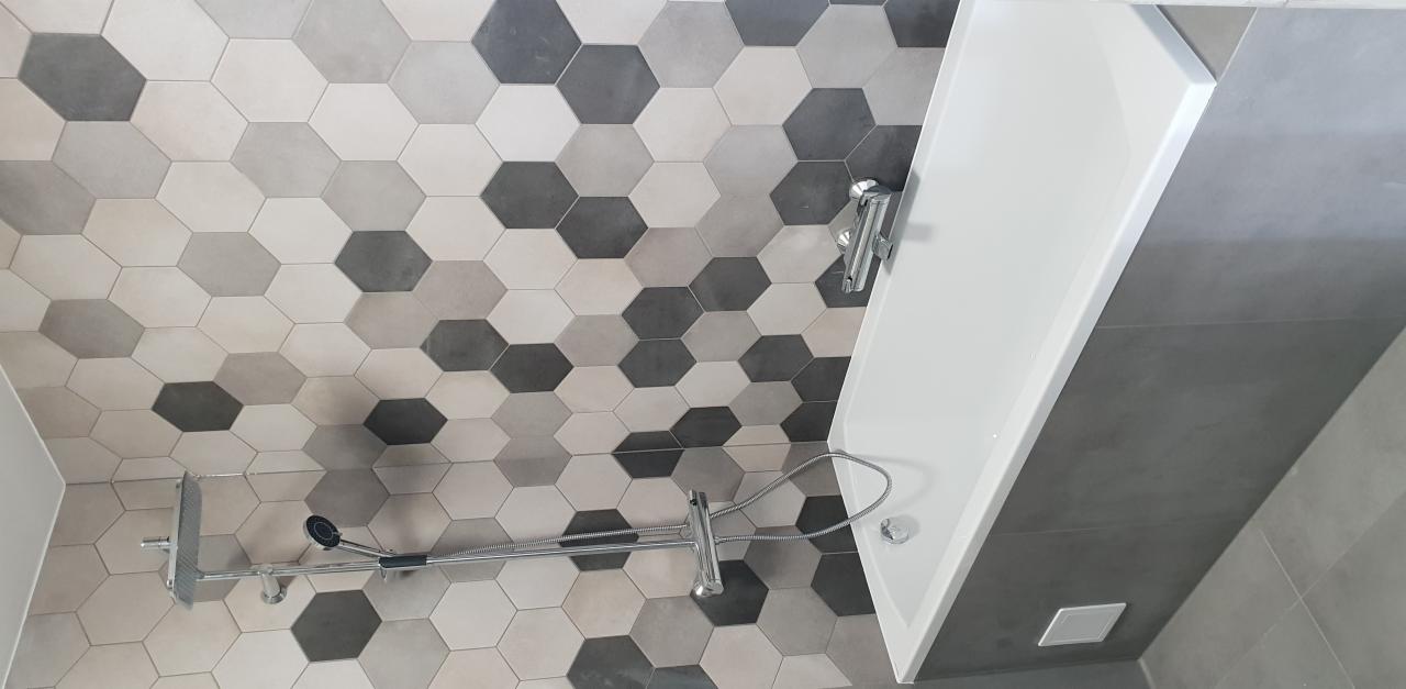 Ukończona łazienka z wanną, armaturą i heksagonalnymi płytkami w odcieniach szarości na ścianie.