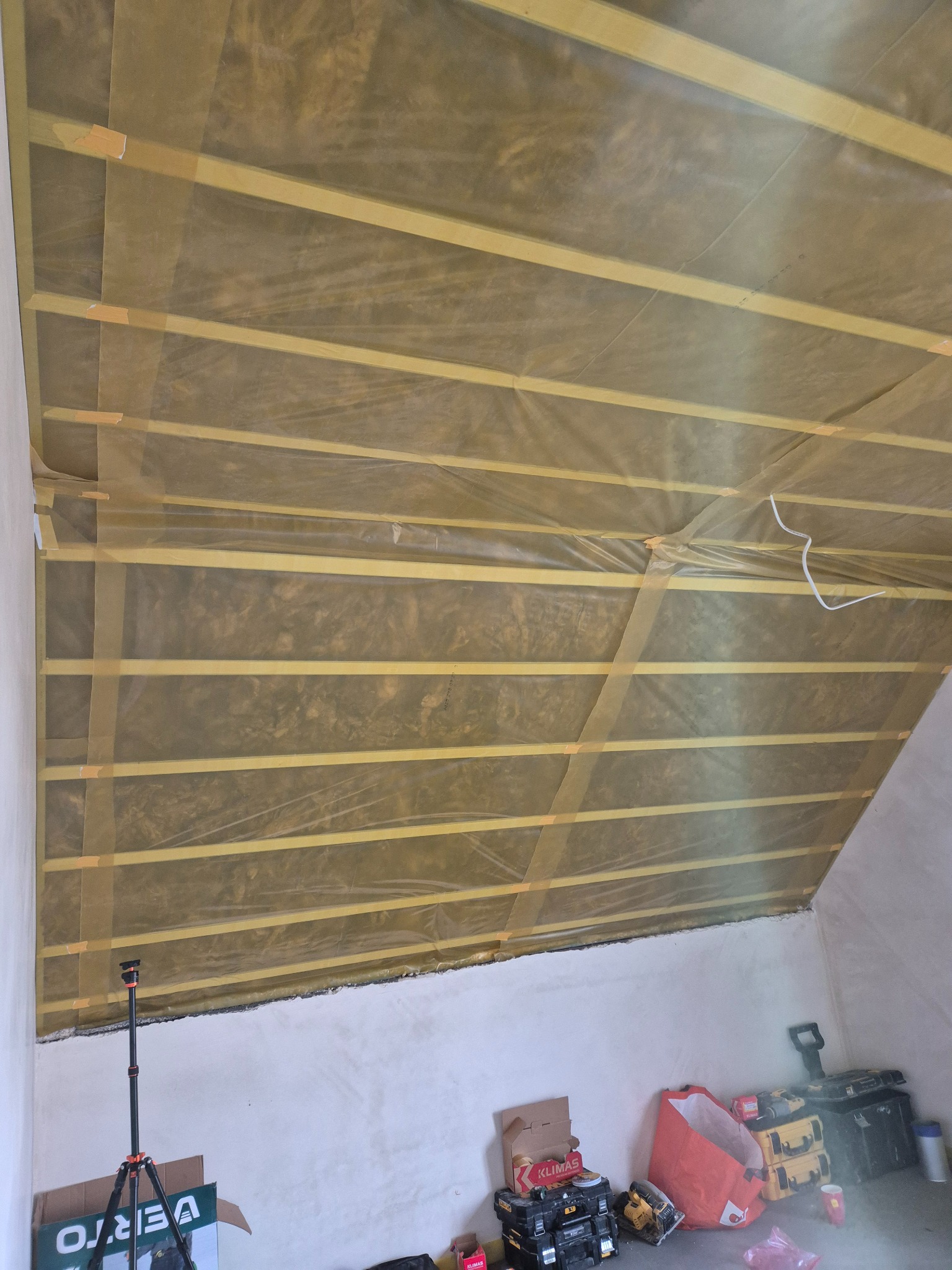 Poddasze w trakcie izolacji: widoczne drewniane belki, wełna mineralna zabezpieczona folią. Na podłodze narzędzia i materiały budowlane. Ujęcie z dołu, szeroki kąt.