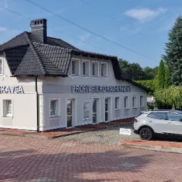 Budynek biura rachunkowego z napisem 'PROFIT BIURO RACHUNKOWE' i adresem 'ŻUCHOWSKA 75A', obok zaparkowany srebrny samochód, w tle zieleń drzew i błękitne niebo.