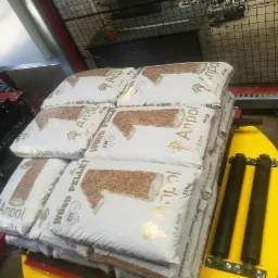Ułożone na palecie worki z pelletem drzewnym marki Anpol, każdy o wadze 15 kg, z widocznym znakiem jakości ENplus A1, na tle linii produkcyjnej.