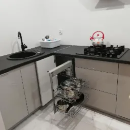 Nowoczesna kuchnia z szarymi frontami, czarnym blatem i wysuwanym cargo z garnkami. Widoczny zlew, płyta gazowa i czajnik w kropki.