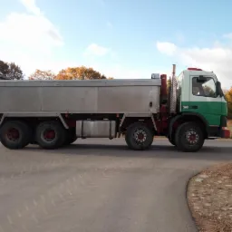Ciężarówka wywrotka Volvo 380 z aluminiową skrzynią ładunkową, stojąca na asfaltowej drodze w jesiennym krajobrazie.