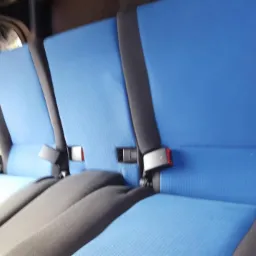 Niebieska tapicerka siedzeń samochodowych z czarnymi pasami bezpieczeństwa i zagłówkami, widok z wnętrza pojazdu.