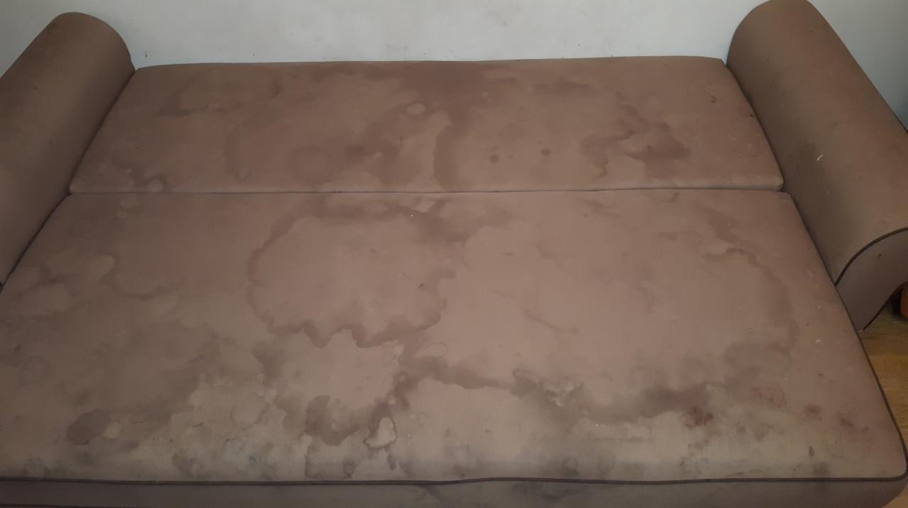 Brązowa kanapa z widocznymi plamami i zabrudzeniami na tapicerce, wymagająca czyszczenia.
