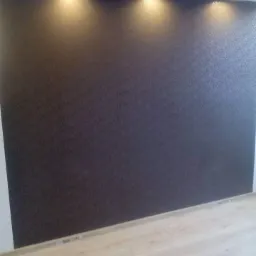 Ciemna ściana z delikatnym wzorem oświetlona punktowymi lampami sufitowymi, jasna podłoga z paneli.