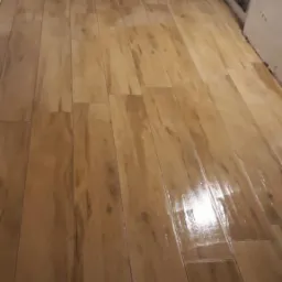 Ułożona, błyszcząca podłoga z płytek imitujących drewno w trakcie remontu, widoczne niedokończone ściany i fragmenty instalacji.