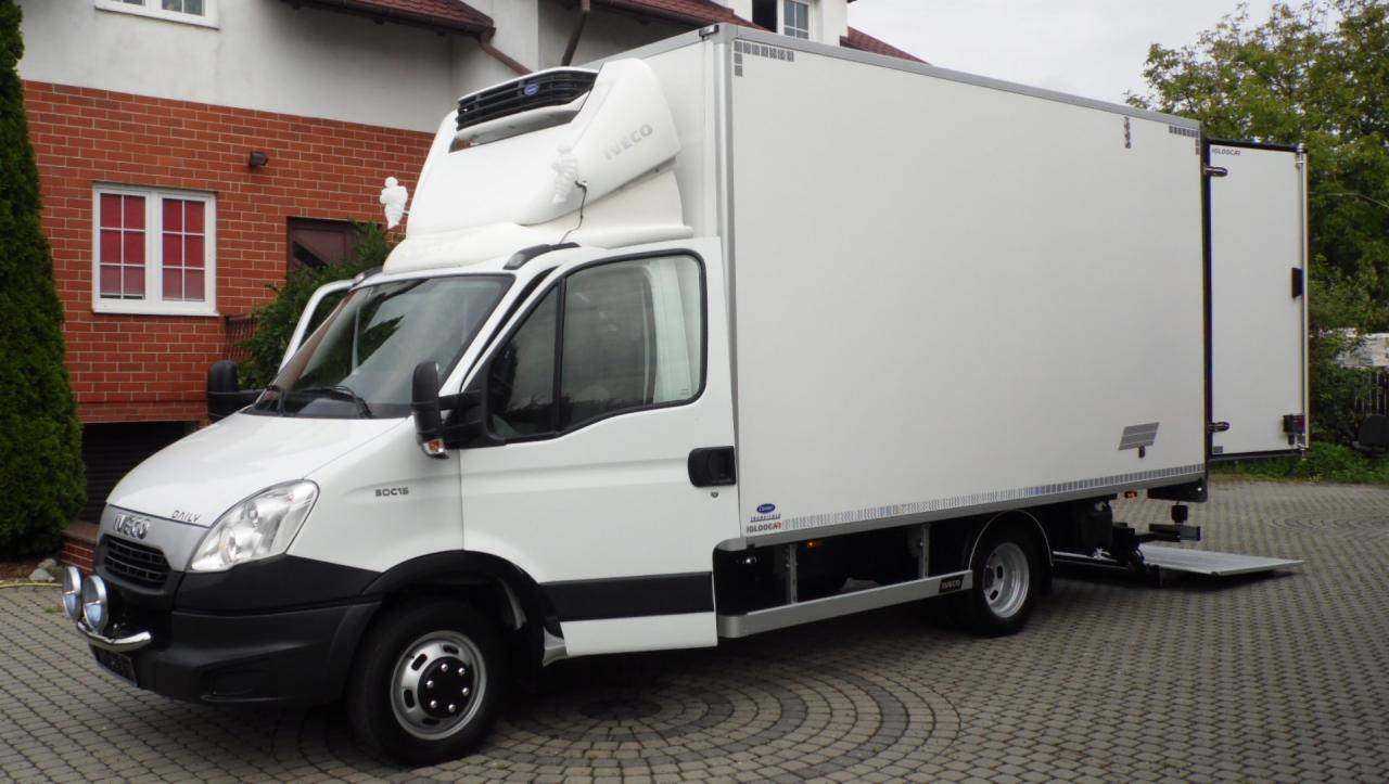 Biały samochód dostawczy Iveco Daily z otwartymi tylnymi drzwiami i rampą załadunkową, zaparkowany na posesji w Warszawie, widok z boku.