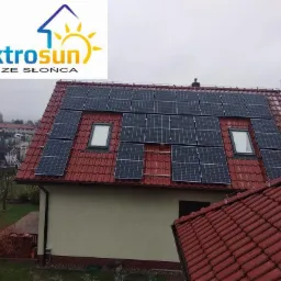 Panele słoneczne na czerwonym dachu domu jednorodzinnego z oknami dachowymi, widok z góry, logo firmy ElektroSun w lewym górnym rogu.