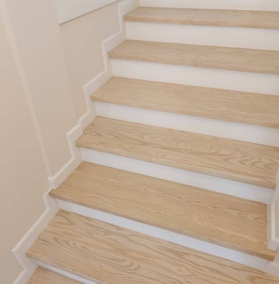 Jasne, drewniane schody z białymi podstopnicami, widok z dołu, delikatne usłojenie drewna.