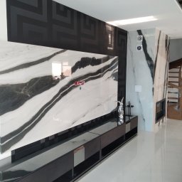 AIRLESS - Nowoczesny salon z marmurową ścianą, czarną konsolą pod telewizorem i drewnianymi schodami w tle, wykończony z dbałością o detale.