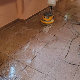 AIRLESS - Maszyna do czyszczenia podłóg marki Tenzi w trakcie pracy na brudnych, brązowych płytkach podłogowych, z widoczną pianą i mokrymi plamami.