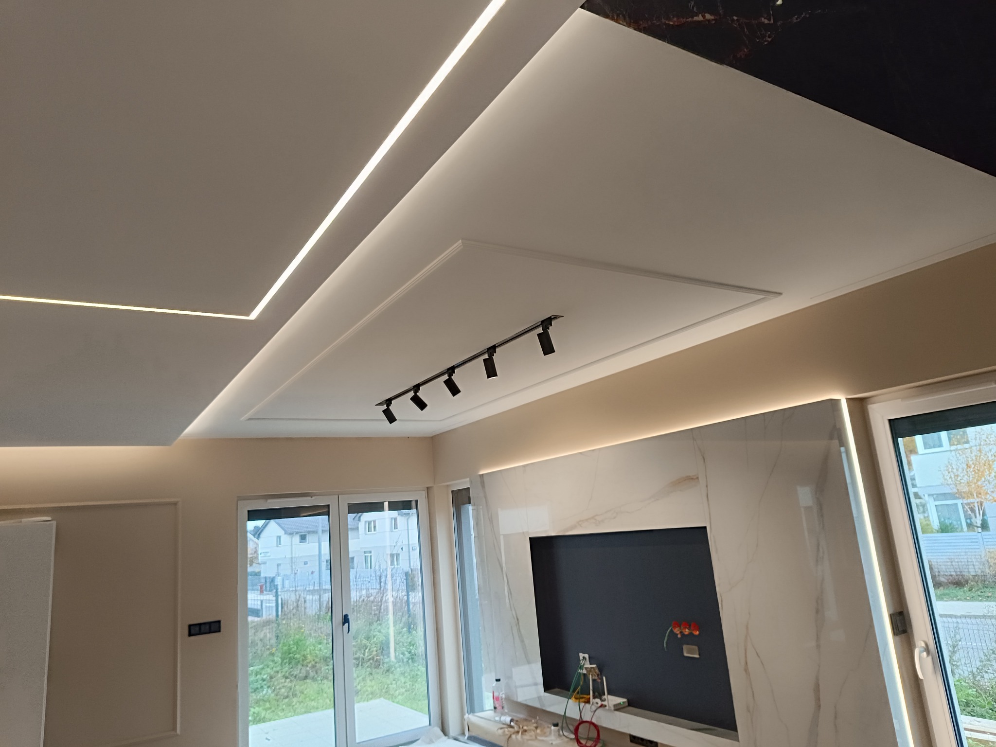 Nowoczesny salon w Szczecinie po remoncie, z podwieszanym sufitem z oświetleniem LED, marmurową ścianą TV i szynoprzewodem z reflektorami.