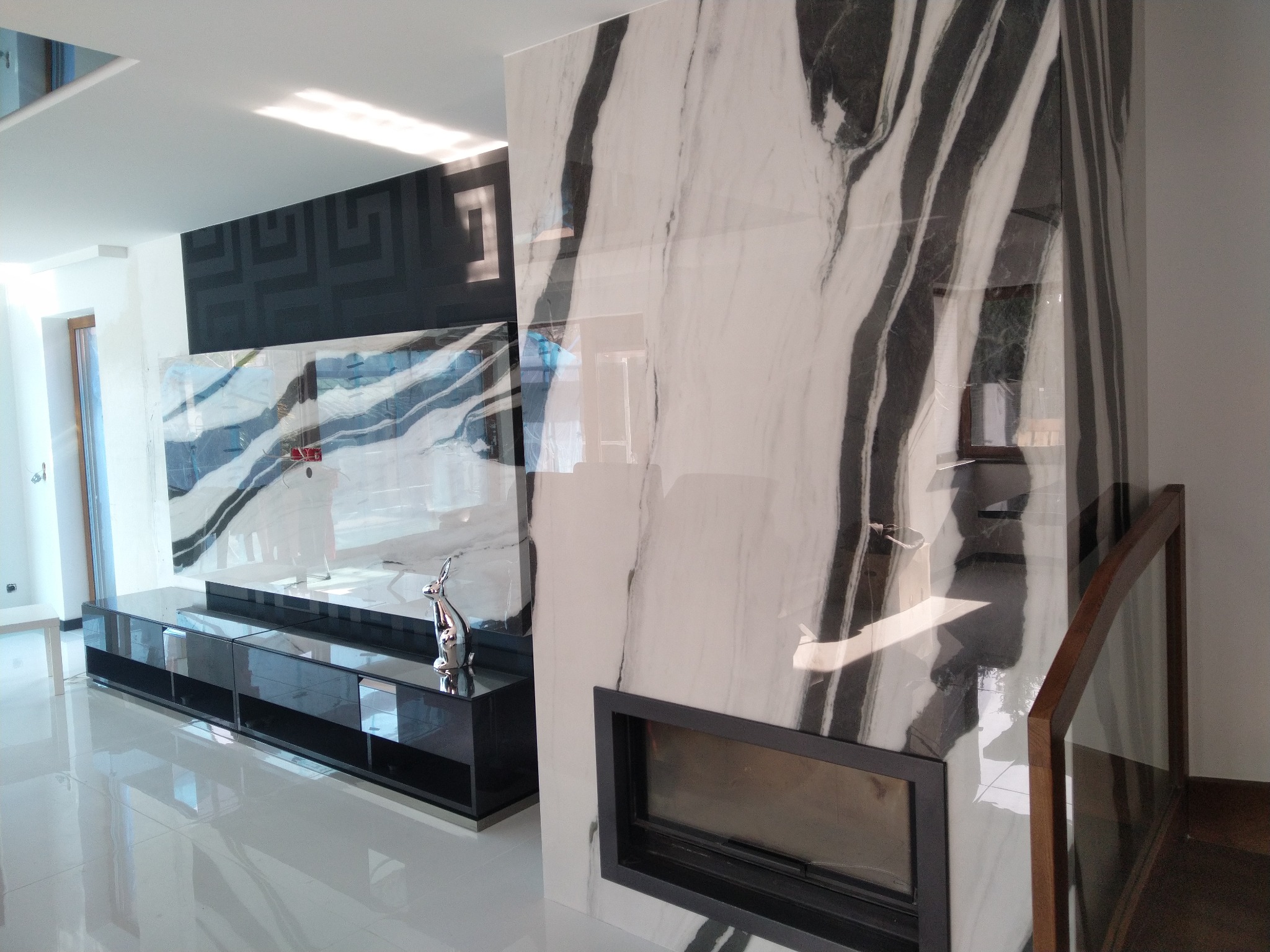 Nowoczesny salon z błyszczącą podłogą, ścianą z marmuru z kominkiem i czarnym panelem dekoracyjnym na ścianie.