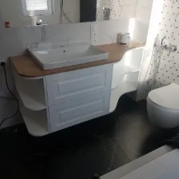 Biała umywalka nablatowa z szafką z szufladami i półkami, drewniany blat, biało-czarne płytki na ścianie, toaleta podwieszana, czarna marmurowa podłoga.