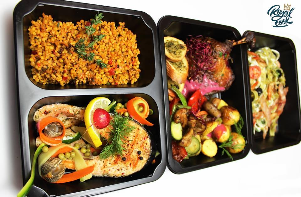 Zestaw posiłków w czarnych pojemnikach: kasza z warzywami, grillowany łosoś z cytryną i muszelkami św. Jakuba, pieczona noga z kaczki z grzankami i warzywami oraz makaron z krewetkami i pesto,...