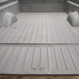 Wnętrze paki samochodu typu pickup po piaskowaniu i pokryciu szarą farbą podkładową, widoczne ślady minimalnej korozji na krawędziach burty.
