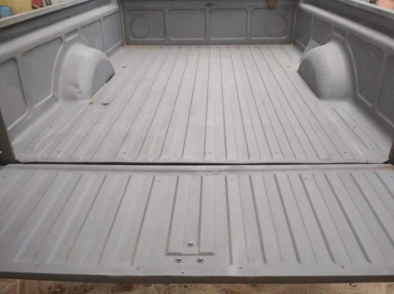 Wnętrze paki samochodu typu pickup po piaskowaniu i pokryciu szarą farbą podkładową, widoczne ślady minimalnej korozji na krawędziach burty.