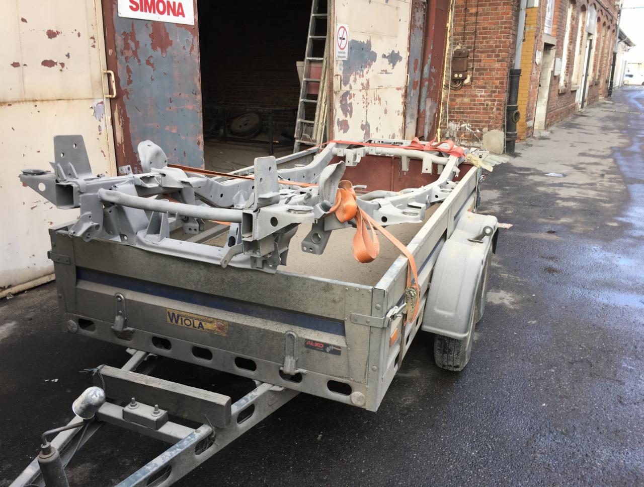 Przyczepa z ramą samochodową po obróbce w Szczecinie, zabezpieczona pasami transportowymi na tle budynku z czerwonej cegły i otwartych wrót warsztatu.