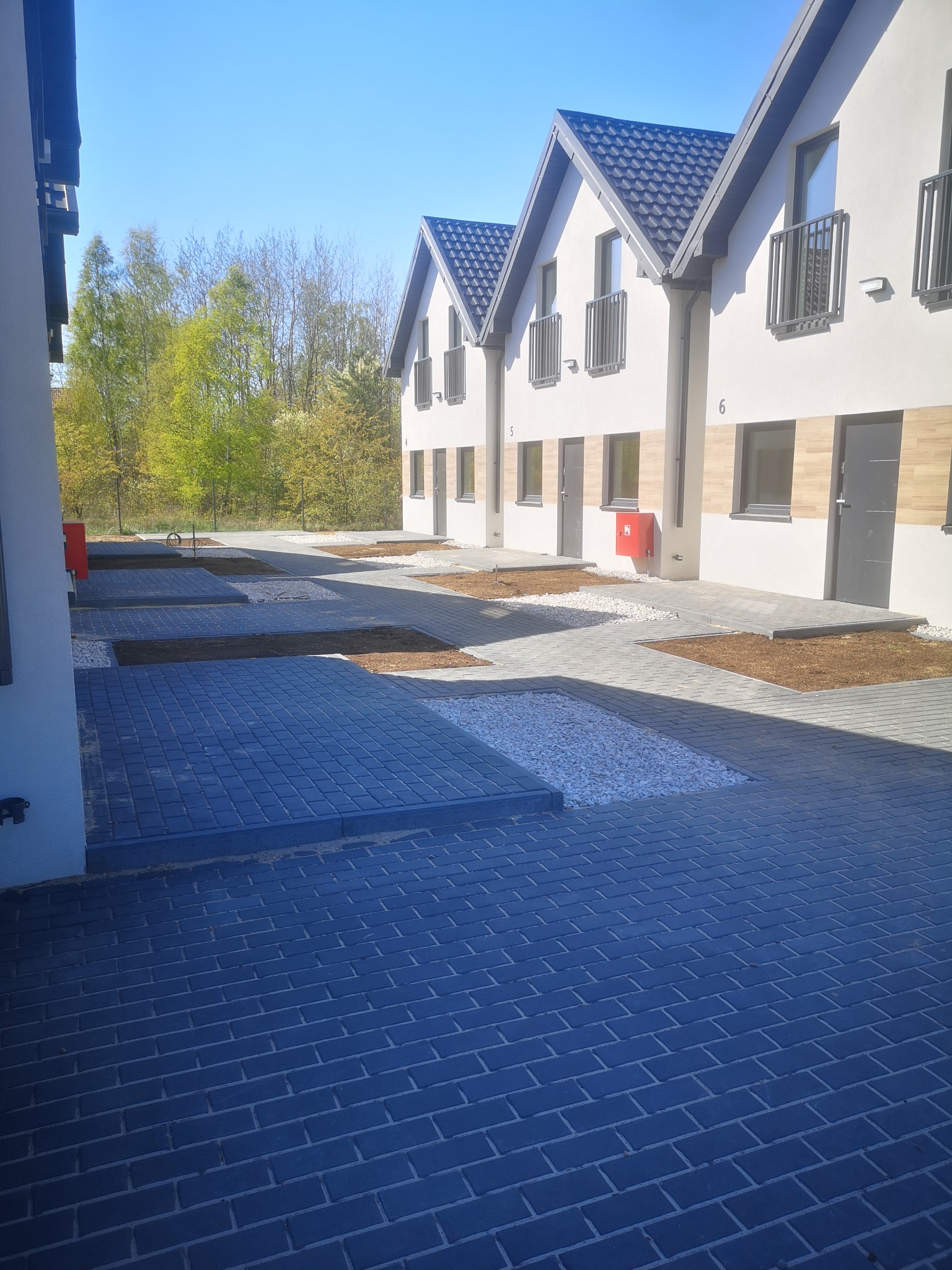 Nowe szeregowe domy z ciemną kostką brukową na podjazdach i białym kamieniem ozdobnym, widok z niskiej perspektywy w słoneczny dzień.