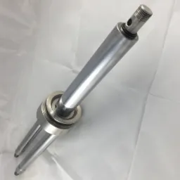 Precyzyjnie obrobiony, metalowy element cylindryczny z gwintem i otworami, leżący na białym tle, prawdopodobnie część maszyny.