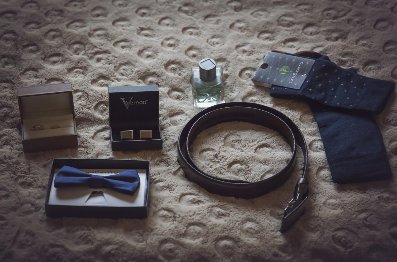Przygotowania ślubne: zestaw męskich akcesoriów na teksturowanym tle - obrączki w drewnianym pudełku, spinki do mankietów w pudełku Vernon, granatowa mucha w pudełku Lancerto, flakon perfum...