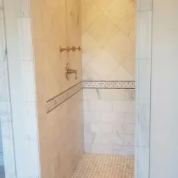 Wykończony prysznic z marmurowymi płytkami w różnych wzorach, w tym romby i prostokąty, z ozdobnym pasem płytek z małymi, ciemnymi punktami, oraz złotą armaturą.