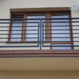 Czarna, metalowa balustrada balkonowa z poziomymi prętami na tle okna budynku.