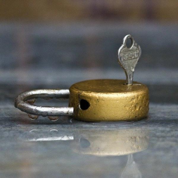 Złoty, okrągły zamek z kluczem w środku, odbity w błyszczącej powierzchni.