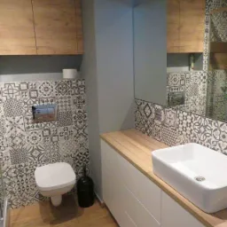 Nowoczesna łazienka z płytkami w stylu patchwork, drewnianymi szafkami i blatem oraz białą umywalką nablatową.